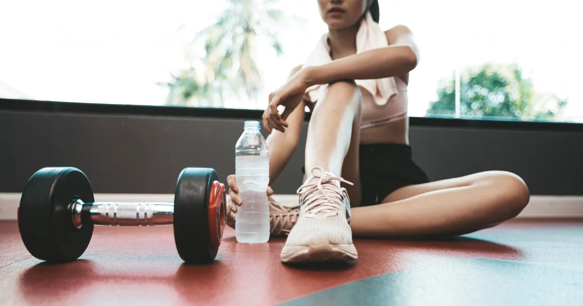 Person training with dumbbells at home next to a pair of running shoes