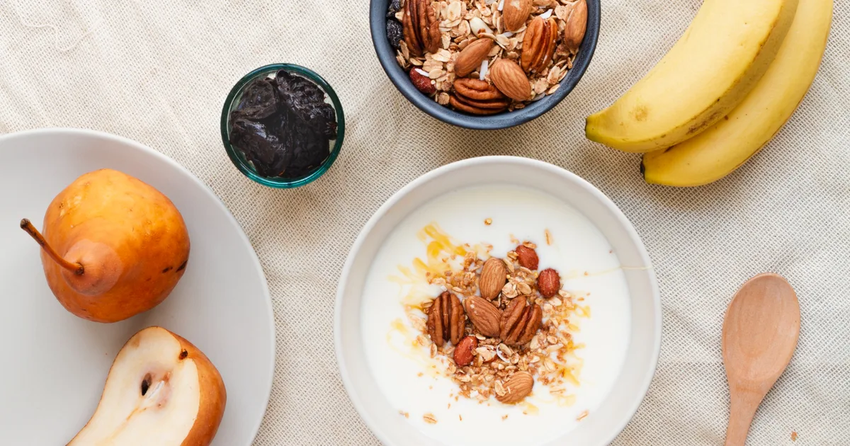 Bol de yogur griego con avena, plátano y frutos secos sobre una mesa de cocina