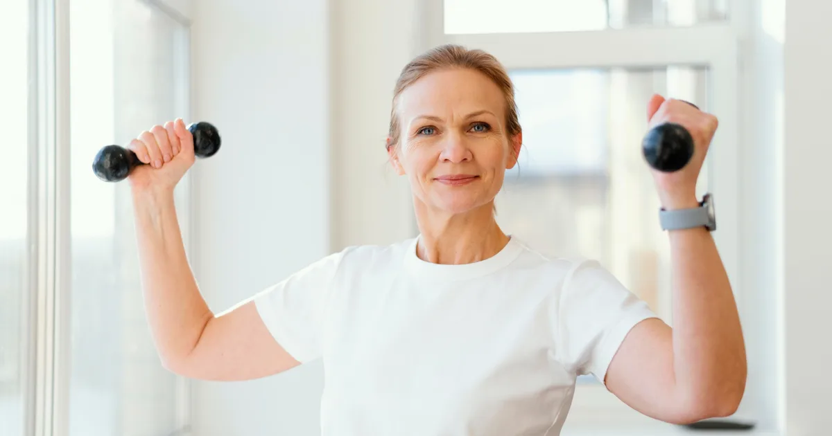 Smiling older woman doing a strength exercise with light dumbbells at home