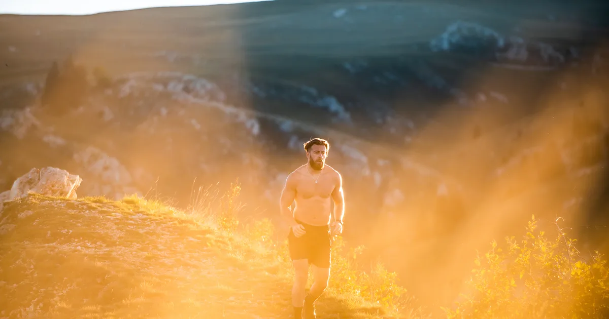 A runner on a trail at sunrise with golden low light and long shadows