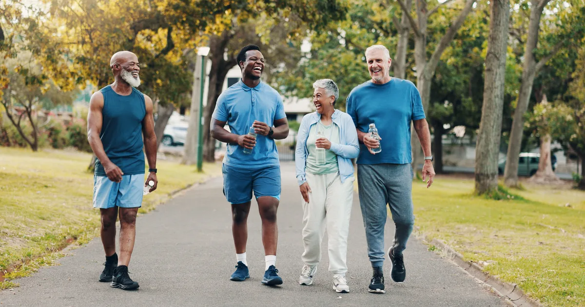 A group of adults walking briskly together through a park on a sunny morning