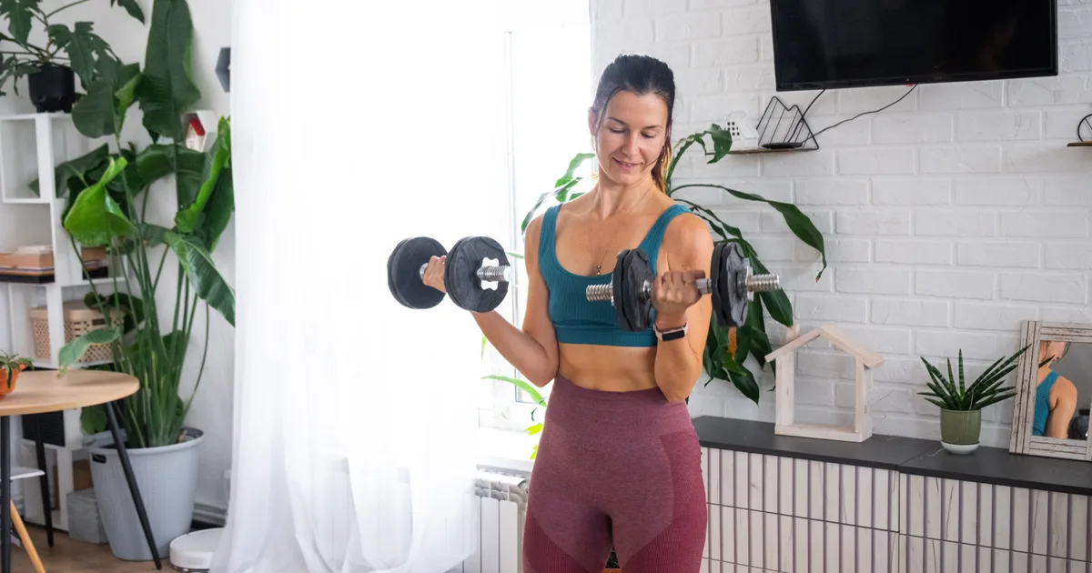 Woman training with dumbbells in her living room at home